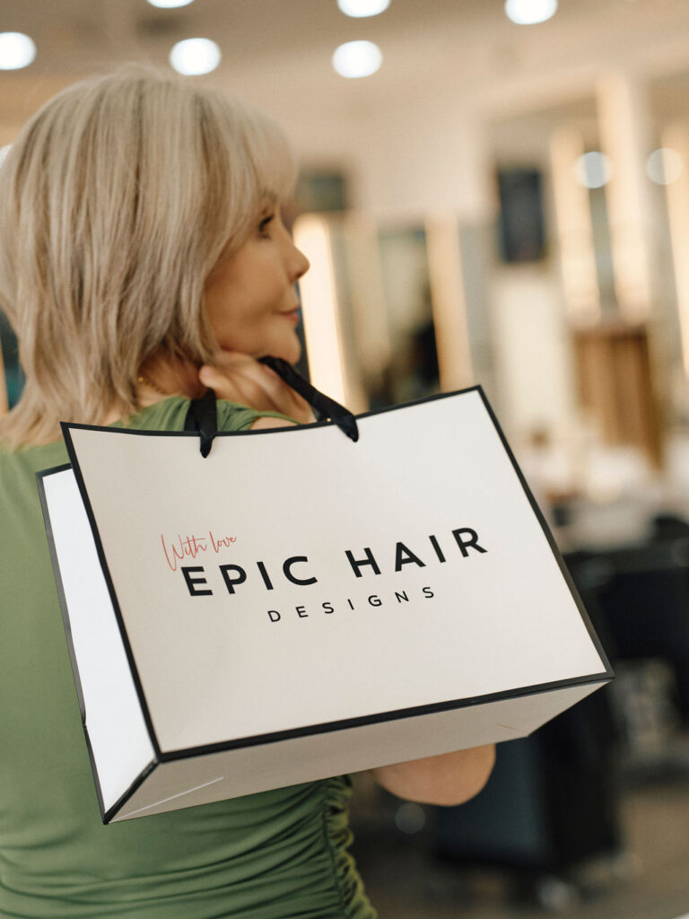Client holding an Epic Hair Designs bag after a blonde hair appointment in salon