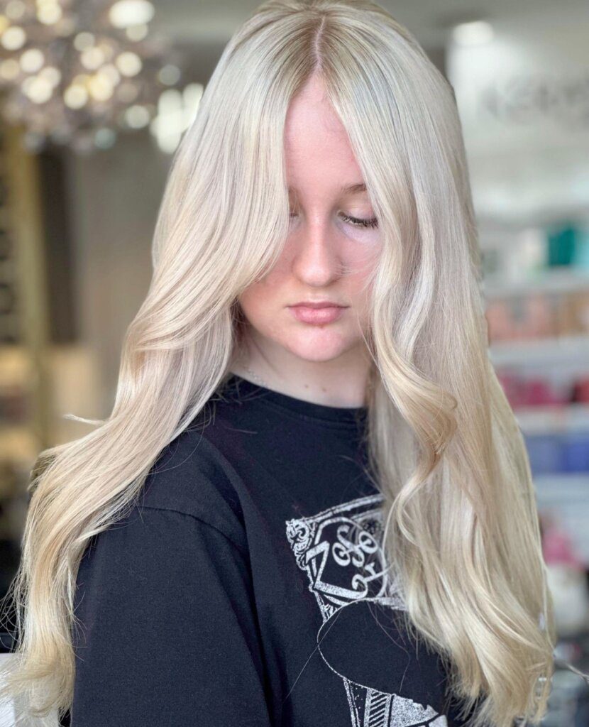 Woman with long, softly waved monochromatic blonde hair featuring seamlessly blended cool and creamy tones.