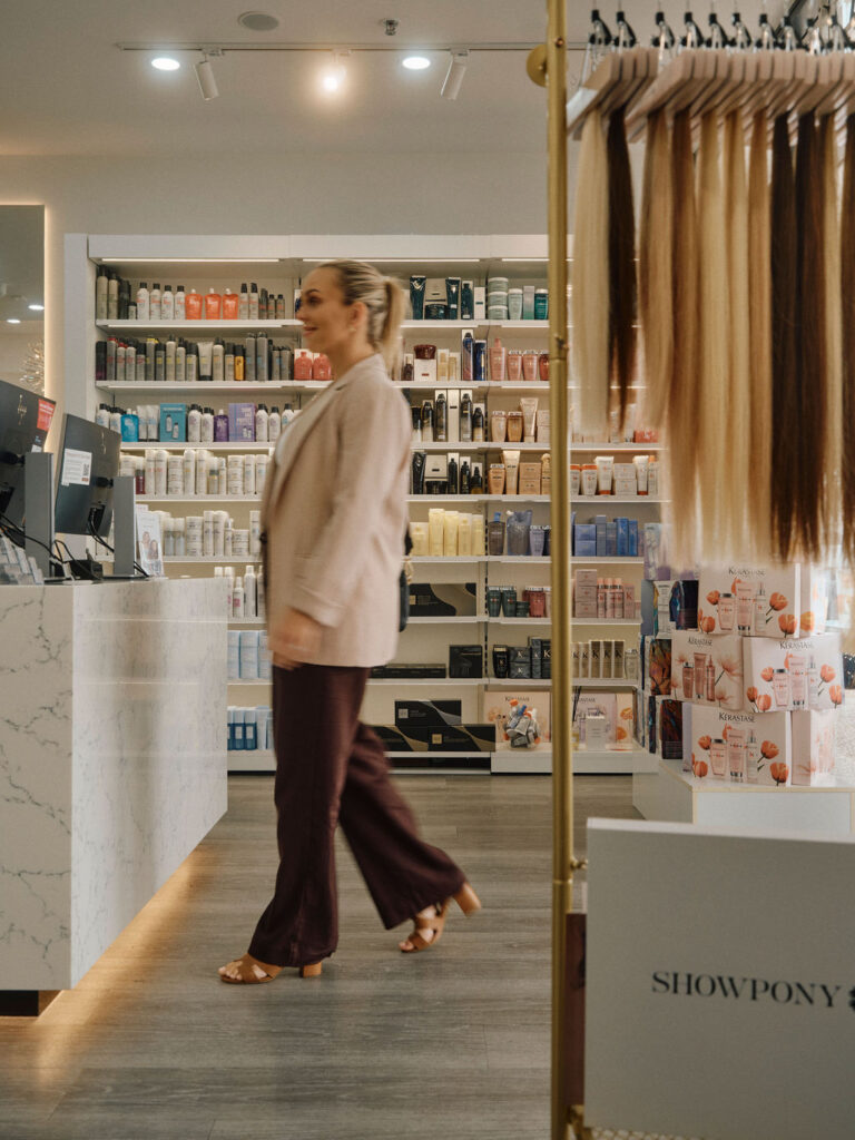 Hairdresser walking through an Epic Hair Designs salon with professional hair extensions on display