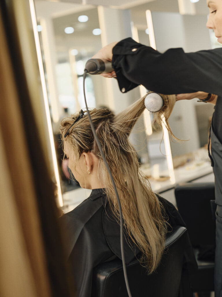 Epic Hair Designs stylist blow drying a client's long blonde hair in salon