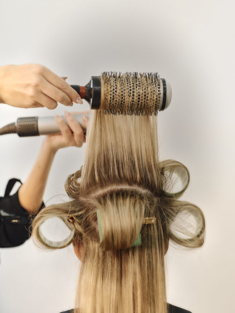Epic stylist using a large round brush while preparing a bouncy blow dry