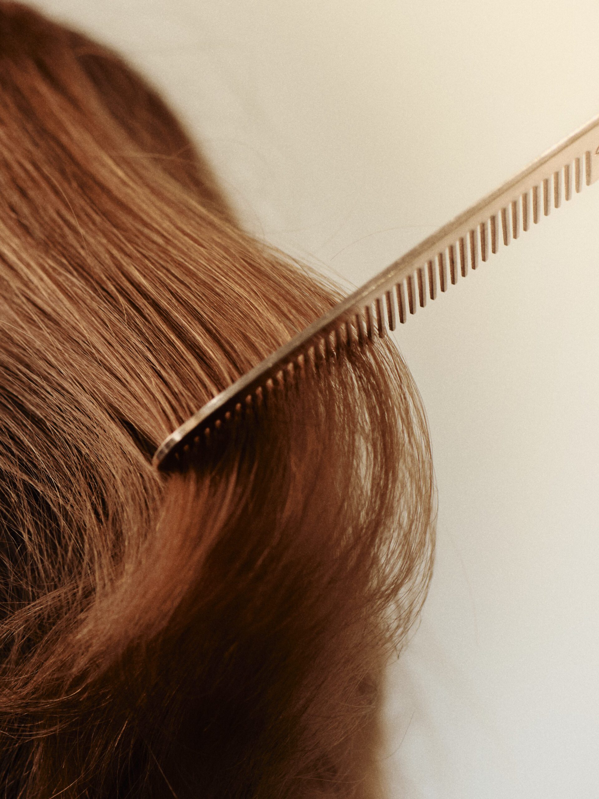 Close view of luminous copper red hair being combed in an Epic Hair Designs salon