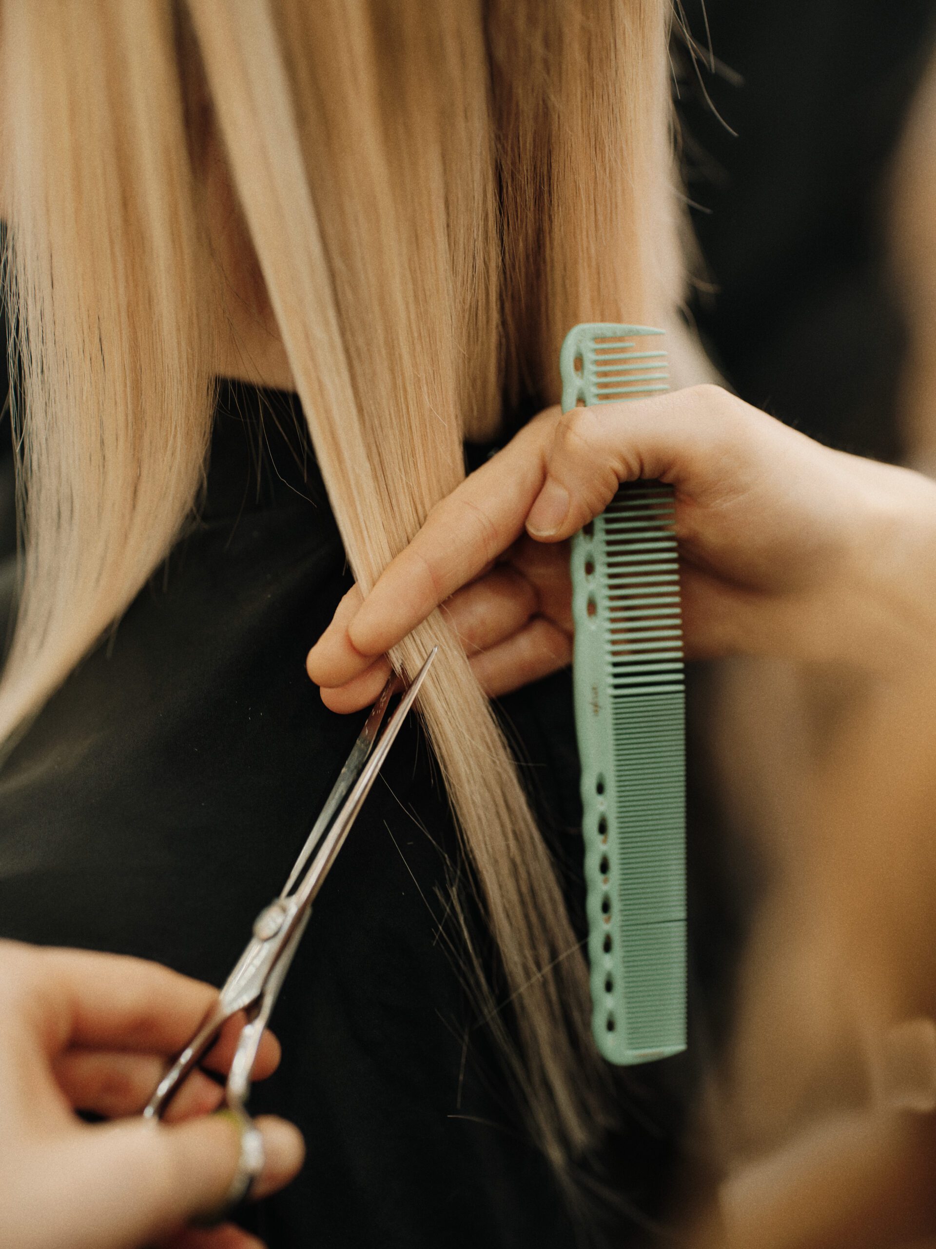 Epic Hair Designs stylist trimming blonde hair with scissors and a comb