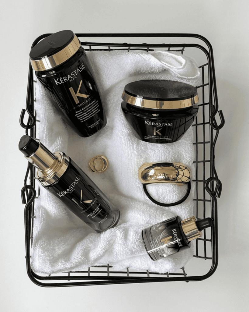 Kérastase Chronologiste haircare products in black and gold packaging arranged on a white towel in a black wire basket.