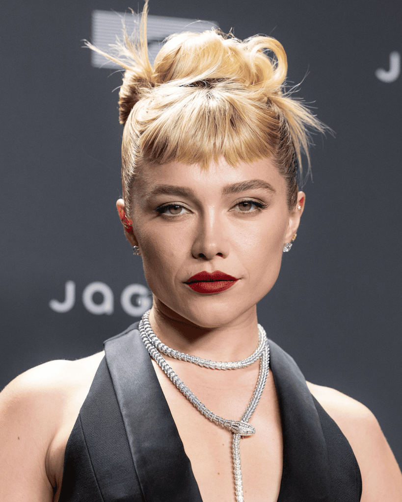 Florence Pugh with short blonde baby bangs and a sculptural updo.